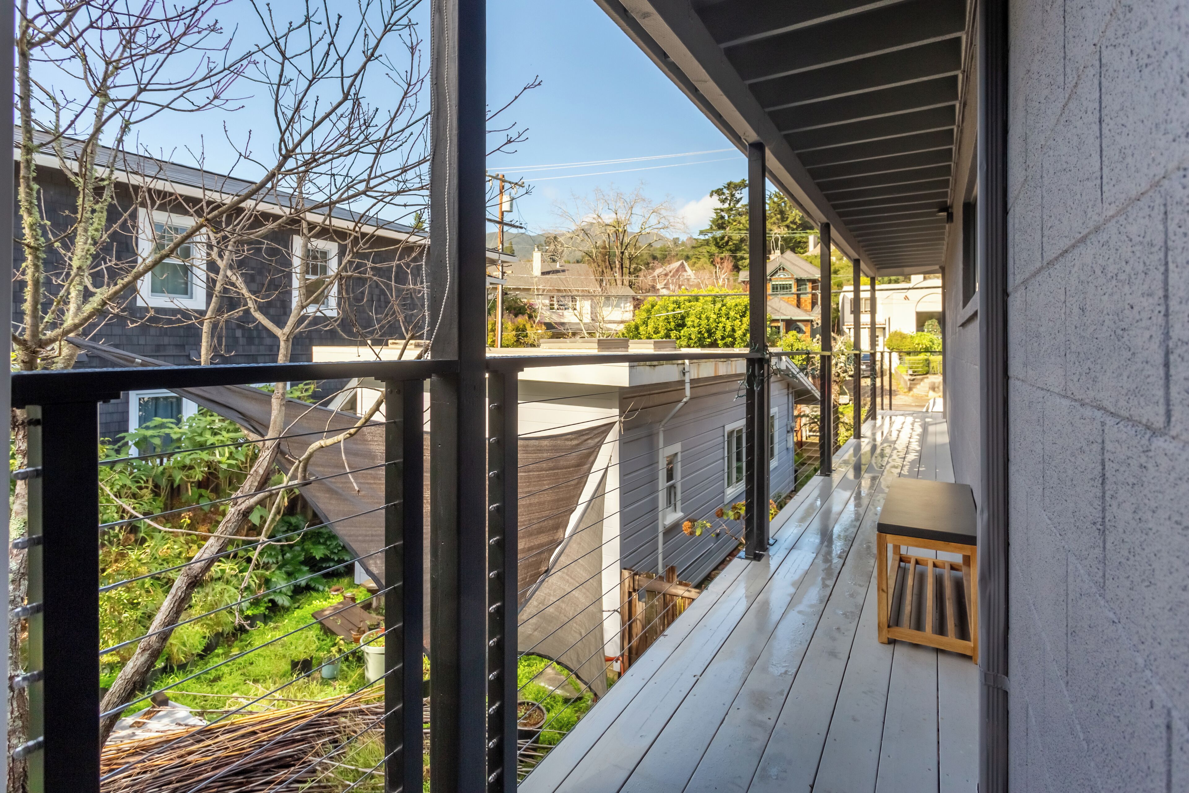 Un espace extérieur abrité, doté d’une terrasse en bois, d’une petite table et offrant une vue sur les maisons voisines et la verdure.