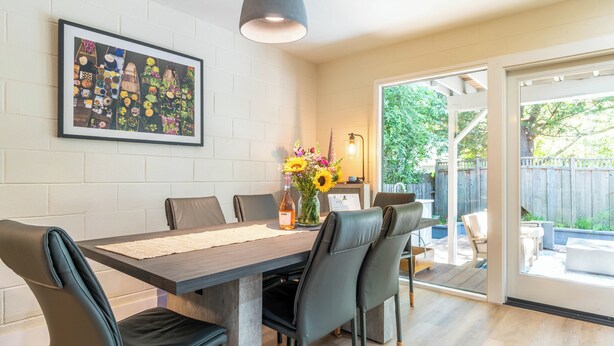 Ein Essbereich mit Tisch, Stühlen, einer Blumenvase und einem gerahmten Bild an der Wand.