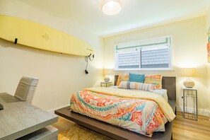 Un dormitorio con cama, una tabla de surf en la pared, una ventana con persianas y una lámpara en una mesita de noche.