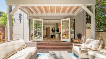 An open patio with a covered seating area, a wooden deck, and a view into the house.