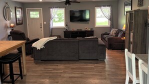 A spacious living room with a large sectional sofa, a dining table with chairs, a TV mounted on the wall, and a ceiling fan. - Quiet 3-bedroom home on 4 aces near Lake Sullivan (Sullivan)