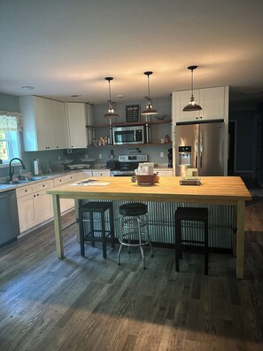 Een moderne keuken met witte kasten, roestvrijstalen apparatuur en een houten kookeiland met barstoelen.