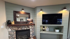 A living room with a stone fireplace, a mounted television, and a shelf with decorative items.