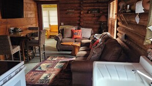 L’intérieur d’un chalet accueillant, avec un coin repas en bois, un canapé, une table basse et une baignoire blanche.