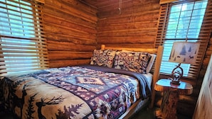 Une chambre confortable dans un chalet en rondins, avec un lit, un ventilateur de plafond et une lampe sur une table de chevet.
