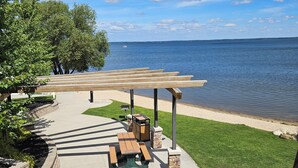 Un patio frente al agua con mesas de picnic y una pérgola que da a un lago.