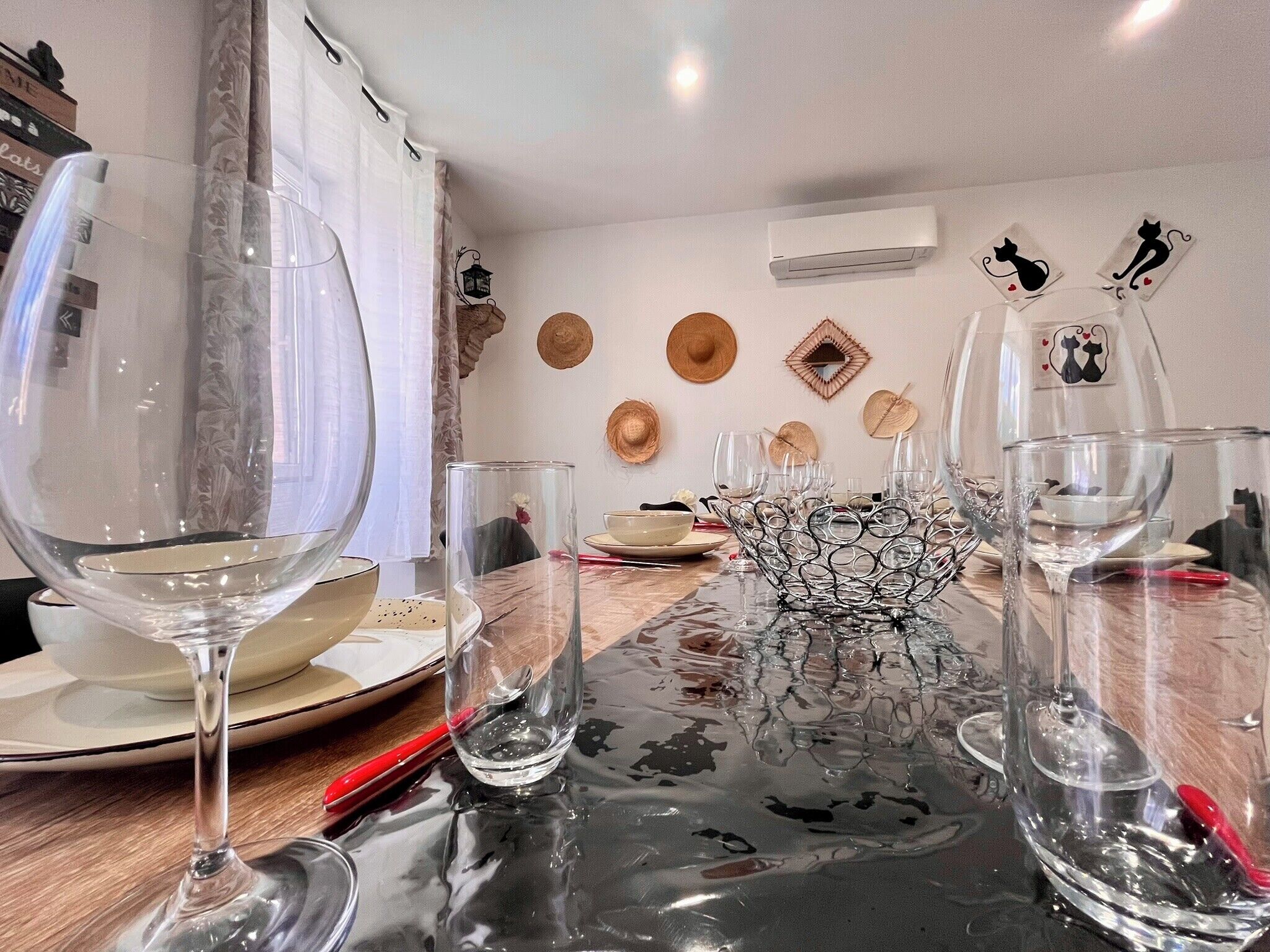 Ett matbord med stilfullt glas och porslin, en dekorativ metallskulptur som mittpunkt och en vägg prydd med hattar och en luftventil med kattmotiv.