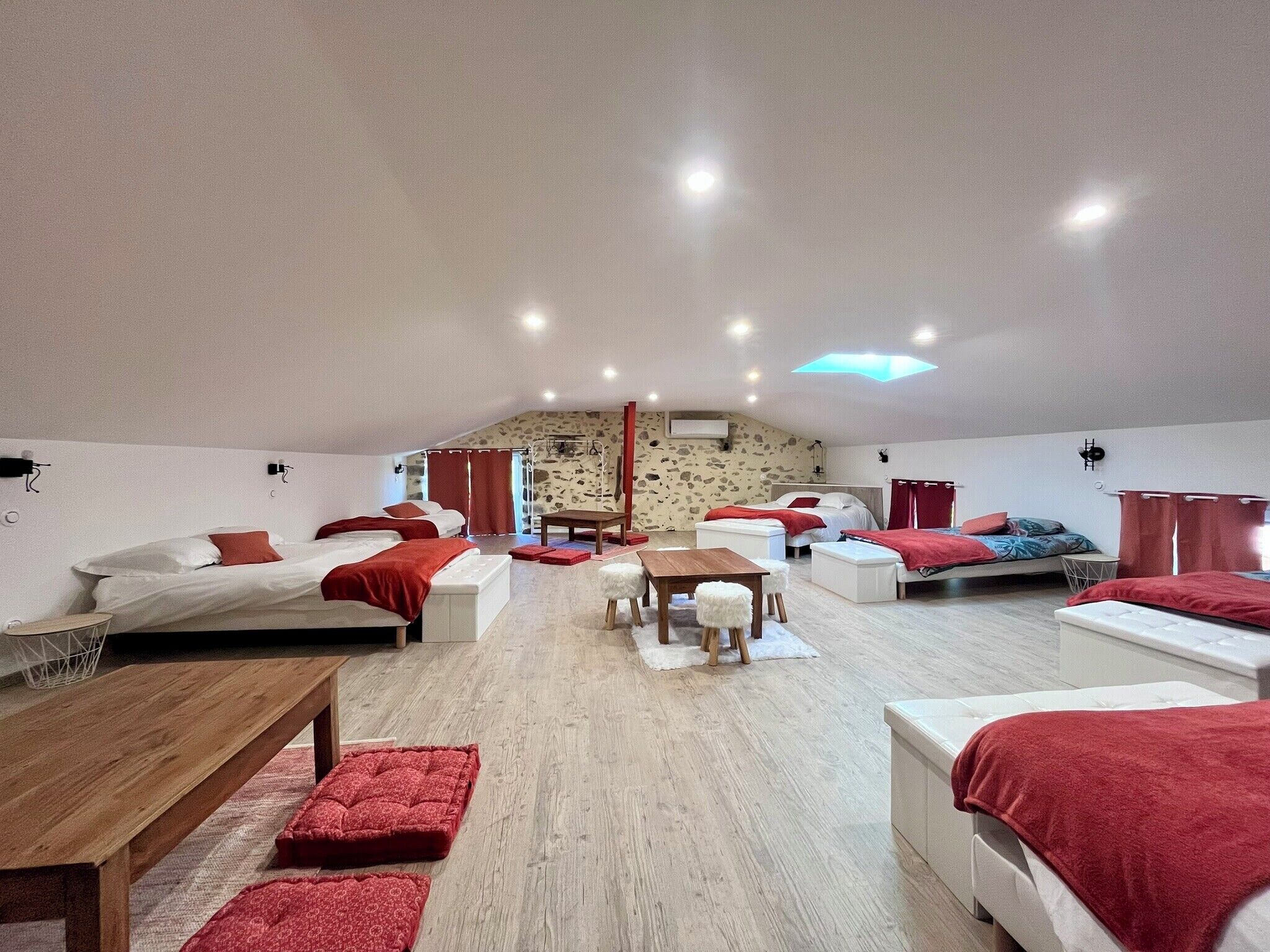 A spacious room with multiple beds, a wooden table, and a stone wall.