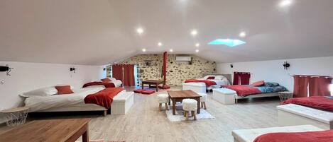 A spacious room with multiple beds, a wooden table, and a stone wall.