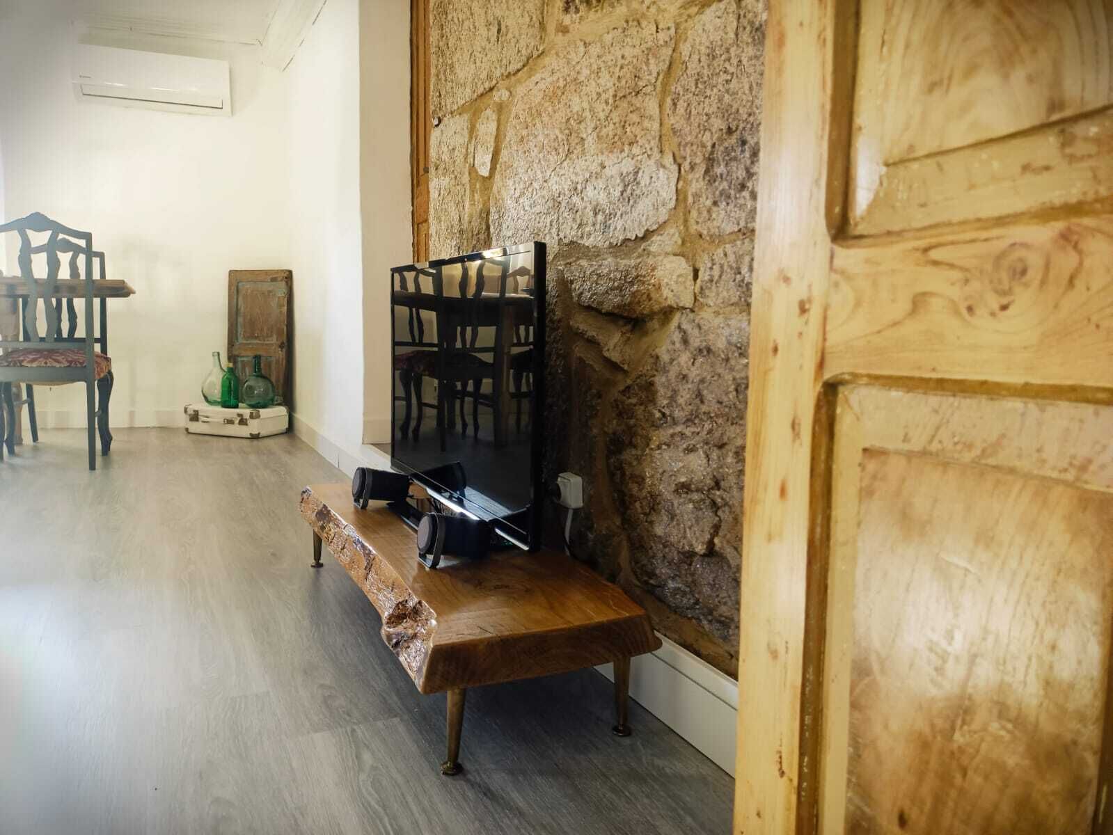 Una habitación con pared de piedra, un banco de madera, un televisor y una mesa con sillas.