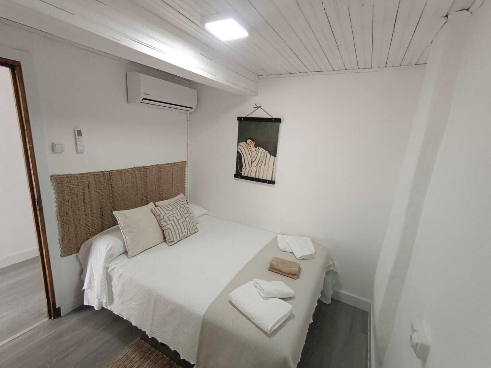 A bedroom with a bed, a hanging artwork, and an air conditioning unit.