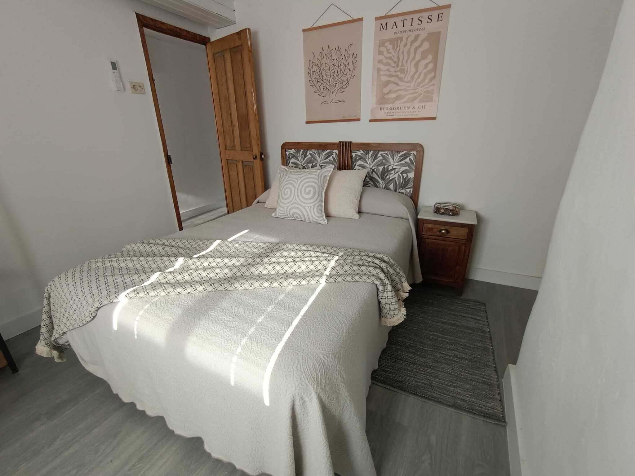 Une chambre à coucher comprenant un lit, une table de chevet, une porte en bois et deux œuvres d’art murales.
