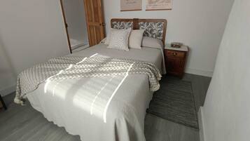 Une chambre à coucher comprenant un lit, une table de chevet, une porte en bois et deux œuvres d’art murales.