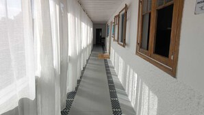 Um corredor com paredes brancas, janelas com moldura de madeira e piso de azulejos.