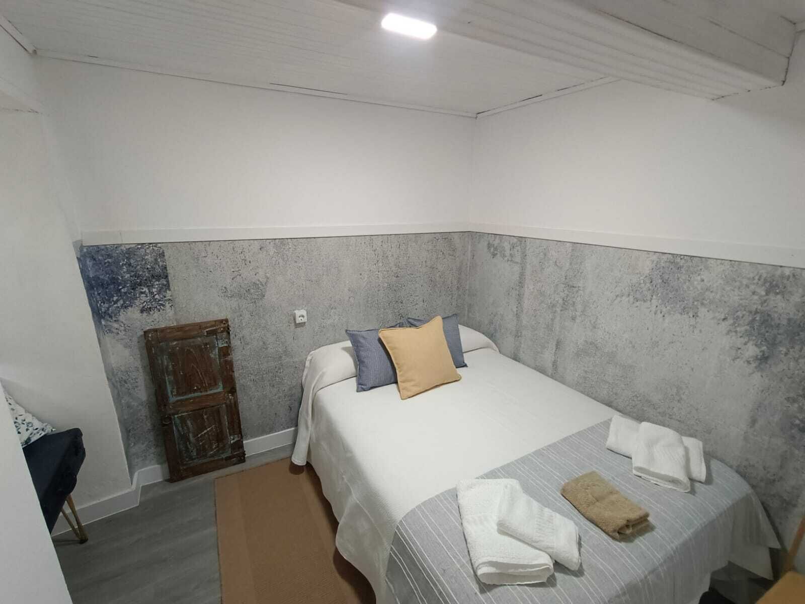 Ein kleines, ordentlich eingerichtetes Schlafzimmer mit einem Einzelbett, einer Holztür und einem kleinen Tisch.