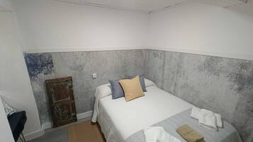 Ein kleines, ordentlich eingerichtetes Schlafzimmer mit einem Einzelbett, einer Holztür und einem kleinen Tisch.