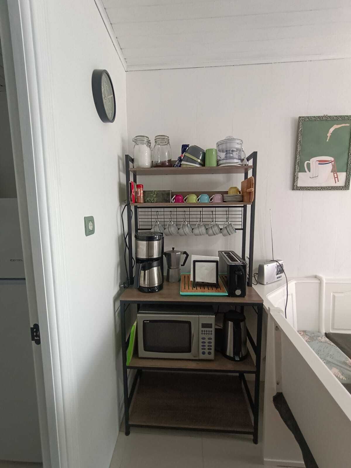 A compact kitchenette with a microwave, toaster, coffee maker, and a shelf with jars and mugs.