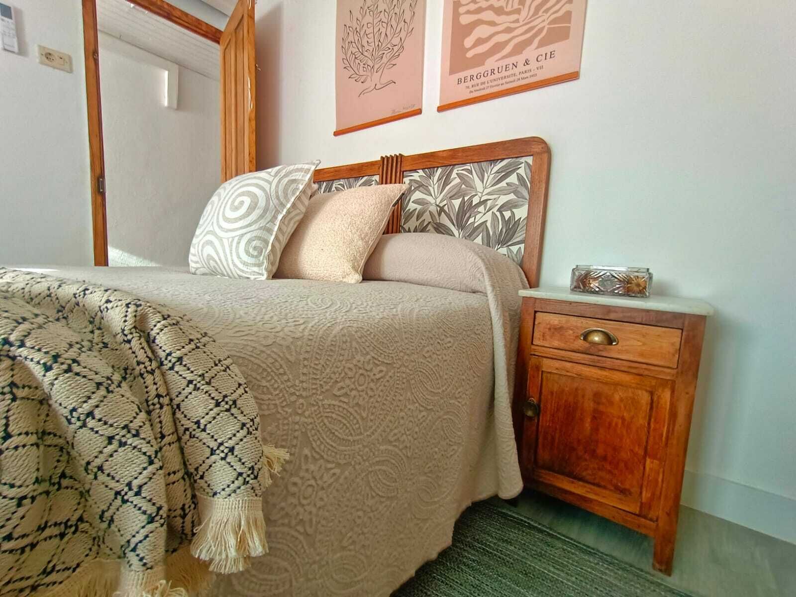 Un dormitorio con cama, almohadas, una mesita de noche y un velador.