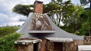 A stone and brick outdoor kitchen with a chimney, surrounded by greenery.