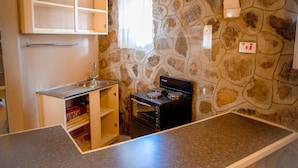Una cocina compacta con pared de piedra, horno empotrado y una pequeña ventana con cortina.