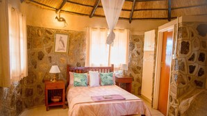 Un dormitorio con pared de piedra, cama con dosel, mesita de noche y puerta de madera.