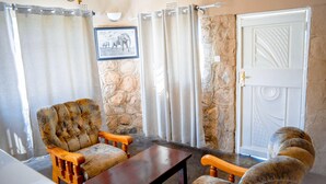A room with a stone wall, a wooden chair, a wooden table, and a door with a decorative panel.