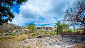 A house with a porch, surrounded by dry grass and trees, under a partly cloudy sky.