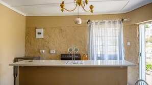 A kitchen with a central island, a chandelier, a stove, and a window with curtains.