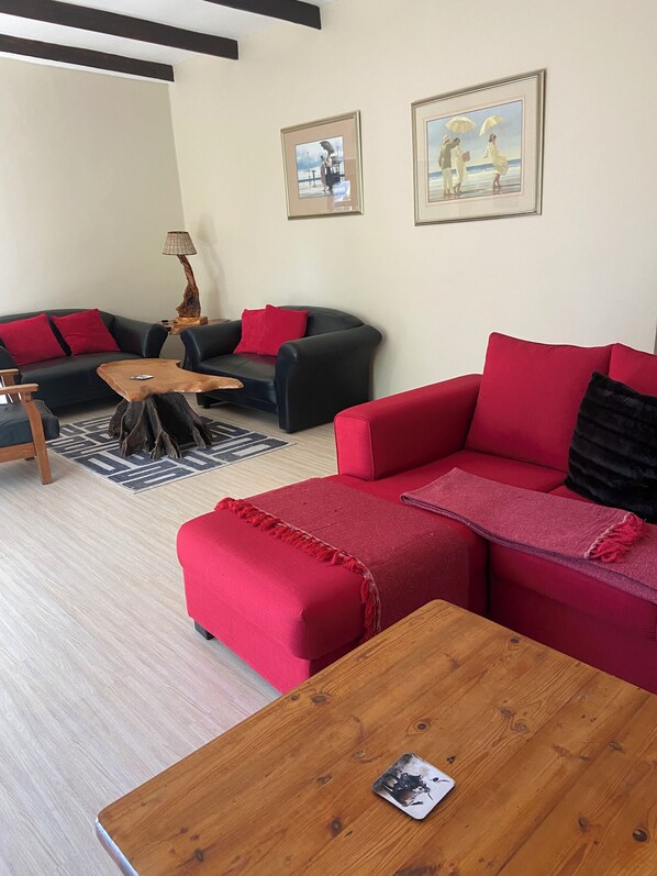 Una sala de estar con un sofá rojo, un sofá negro y una mesa de centro de madera. Hay dos cuadros en la pared y una lámpara sobre una mesita.