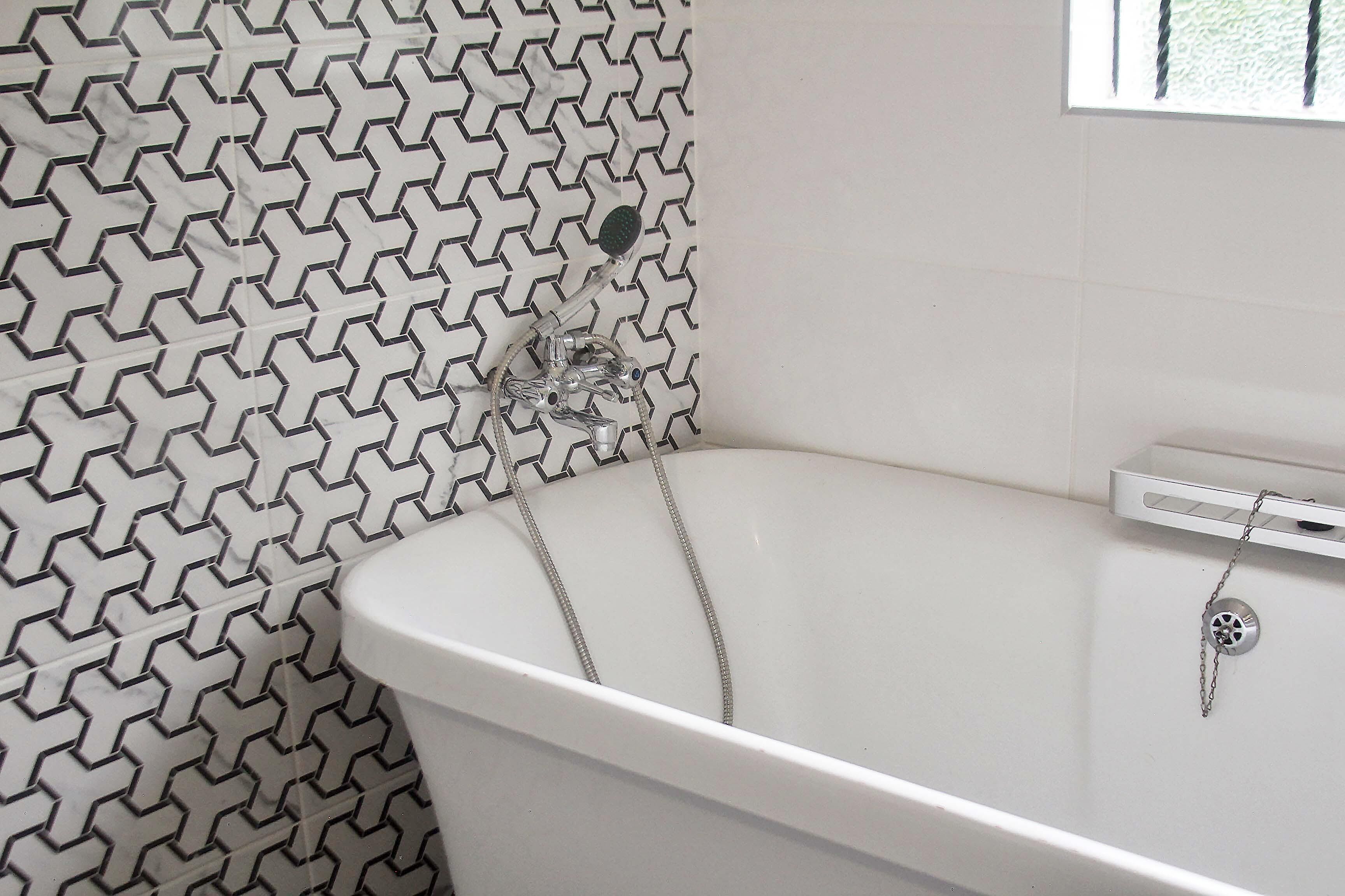 A bathroom with a white bathtub, a showerhead, and a tiled wall with a geometric pattern.
