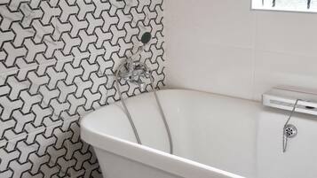 A bathroom with a white bathtub, a showerhead, and a tiled wall with a geometric pattern.