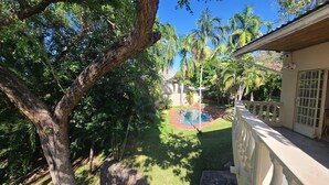 A backyard with a swimming pool, surrounded by lush greenery and palm trees.