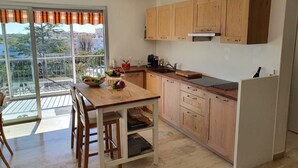 Une cuisine moderne avec des meubles en bois, un îlot central et une porte-fenêtre coulissante donnant sur un balcon.