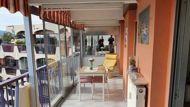 Un balcon avec une table et des chaises, une porte vitrée et une vue sur les bâtiments environnants.
