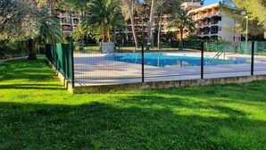 Une piscine entourée d’une clôture verte, avec une pelouse verdoyante et des arbres en premier plan.