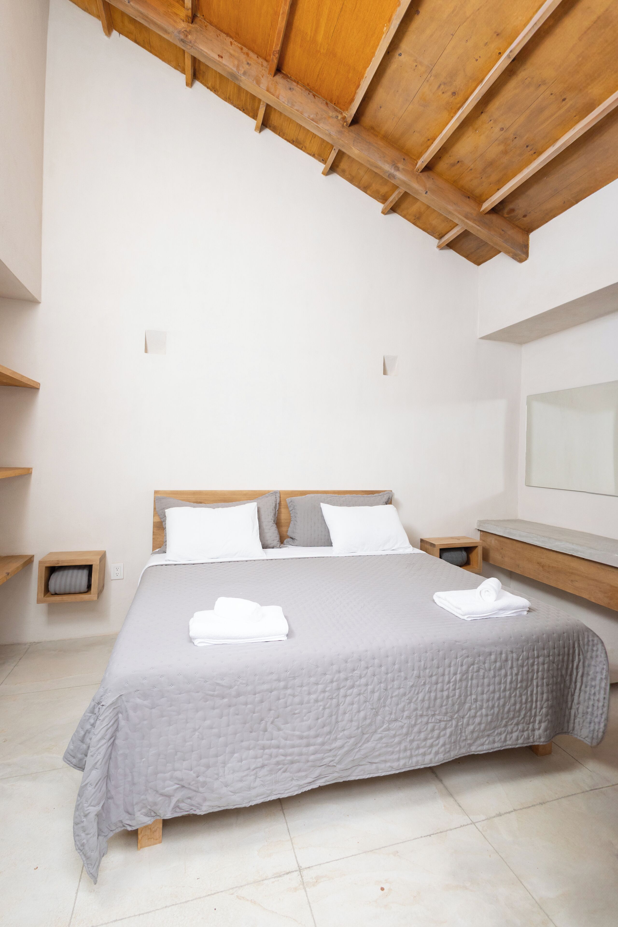 Ein ordentlich eingerichtetes Schlafzimmer mit Bett, Holz-Kopfteil, Nachttischen und einem großen Spiegel.