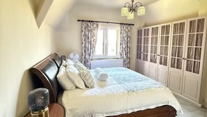 Un dormitorio con una cama grande, una mesita de noche, un ventilador y una ventana con cortinas.