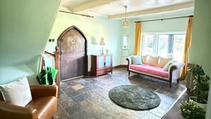 Un salón con suelo a cuadros, una puerta de madera, un sofá, una lámpara y una ventana con cortinas.