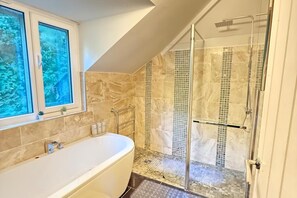Een badkamer met een badkuip, een douchecabine van glas en een raam met uitzicht op groen.