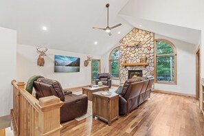 A spacious living room with a stone fireplace, leather sofas, and a large window overlooking greenery.