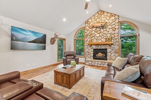 A spacious living room with a stone fireplace, leather sofas, a coffee table, and a large landscape painting.