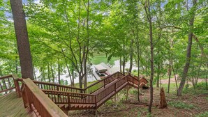 A wooden deck with a staircase leading to a dock by a lake surrounded by trees. - Eagle Ridge (Menomonie)