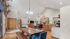 A spacious dining area with a long wooden table and blue chairs, a kitchen with a stone accent wall, and a sign reading 'LAKE HOUST'. - Eagle Ridge (Menomonie)