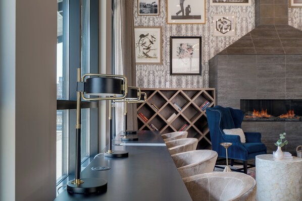 A modern lounge area with a long table, comfortable seating, a fireplace, and a wall decorated with framed artwork. - Sable 203 - Alcove (Minneapolis)