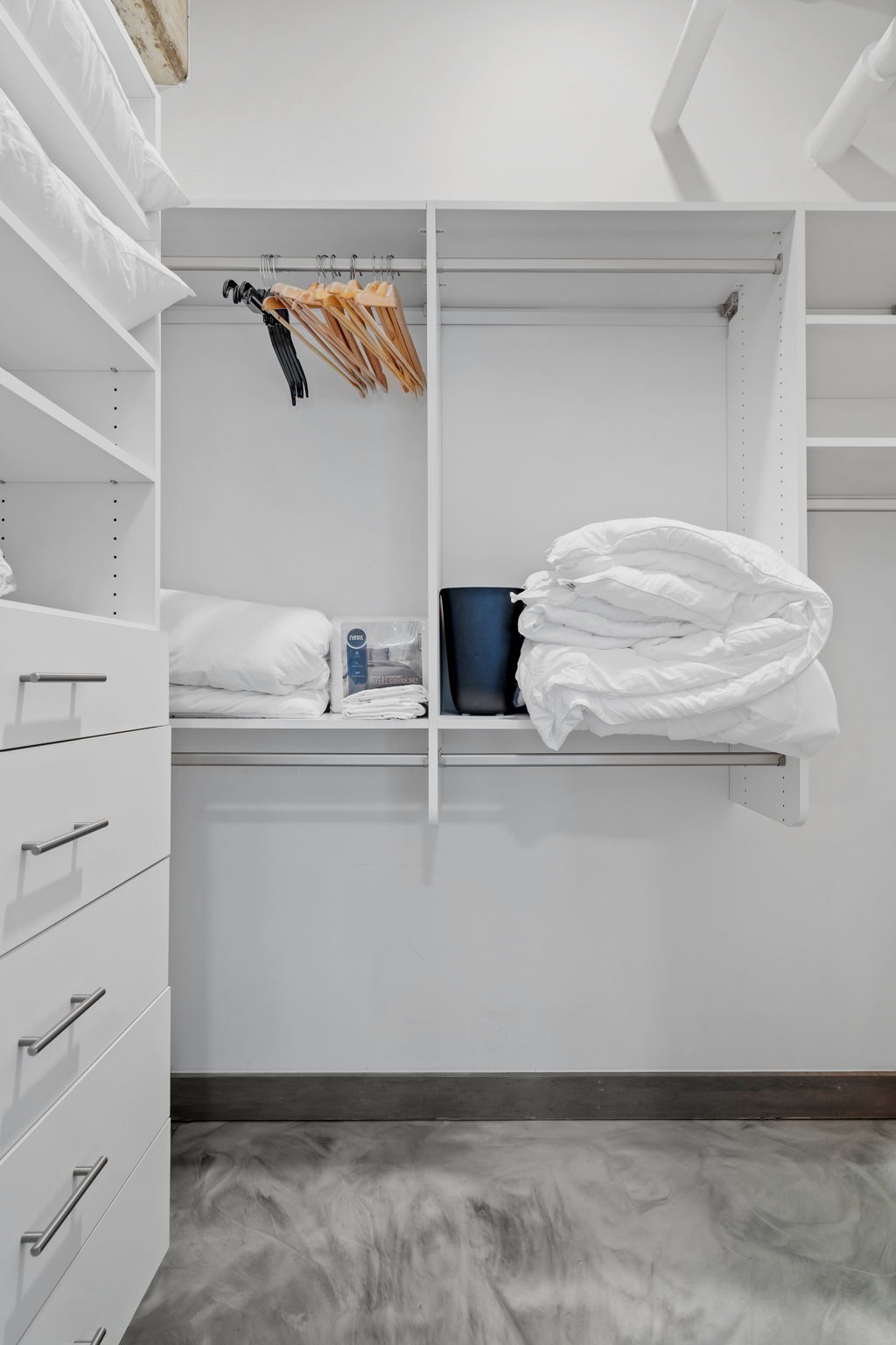 A walk-in closet with shelves, a hanging rod, and a bed with white bedding.