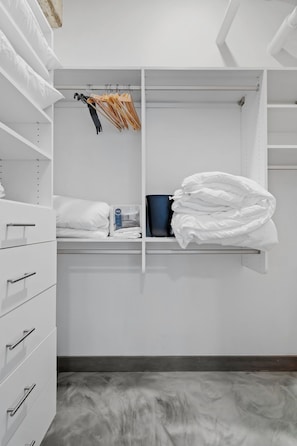 A walk-in closet with shelves, a hanging rod, and a bed with white bedding. - Sable 203 - Alcove (Minneapolis)