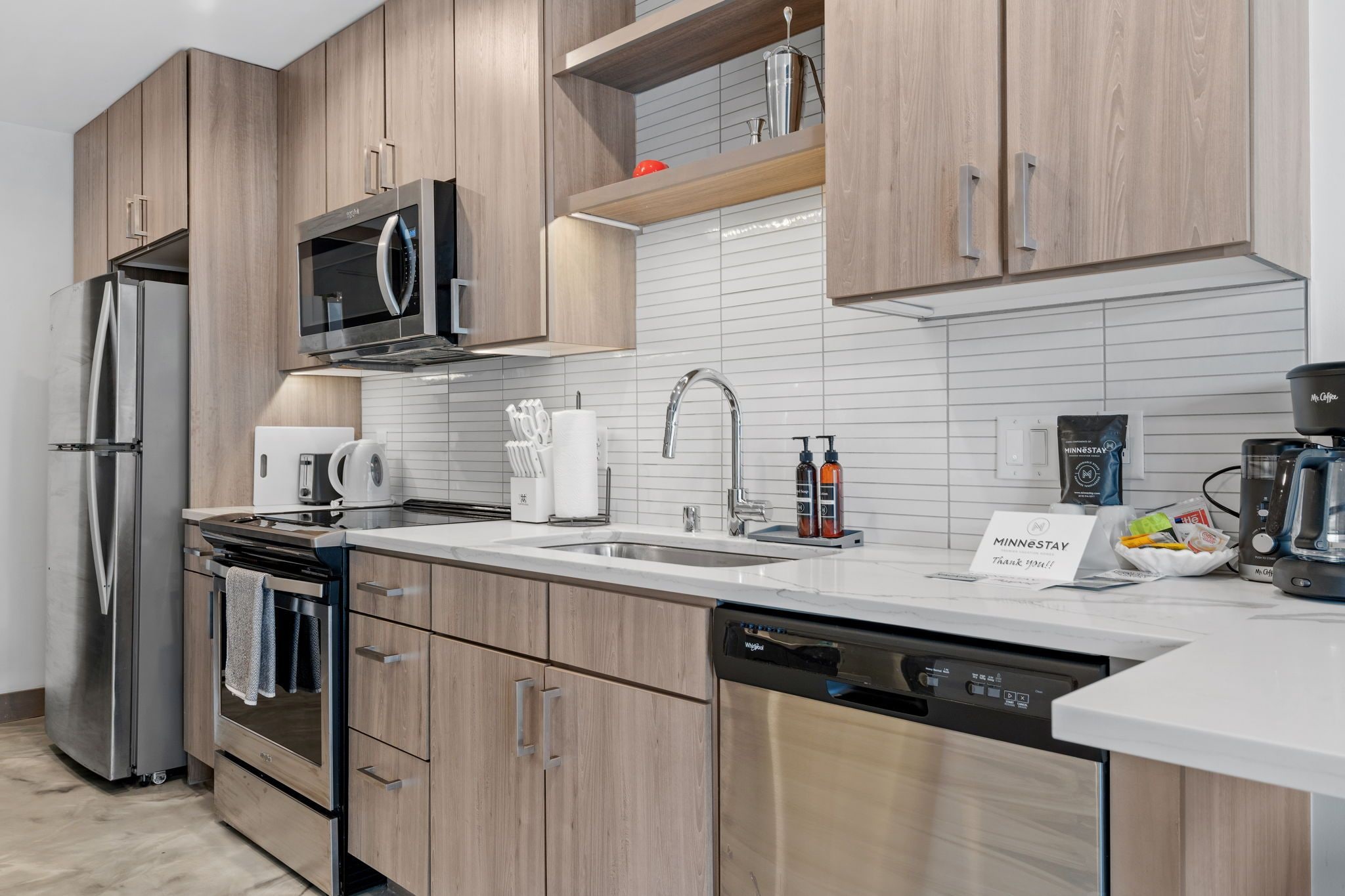 A modern kitchen with stainless steel appliances, wooden cabinets, and a white tiled backsplash.