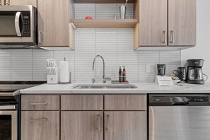 A modern kitchen with a stainless steel sink, wooden cabinets, a microwave, and a coffee maker. - Sable 203 - Alcove (Minneapolis)
