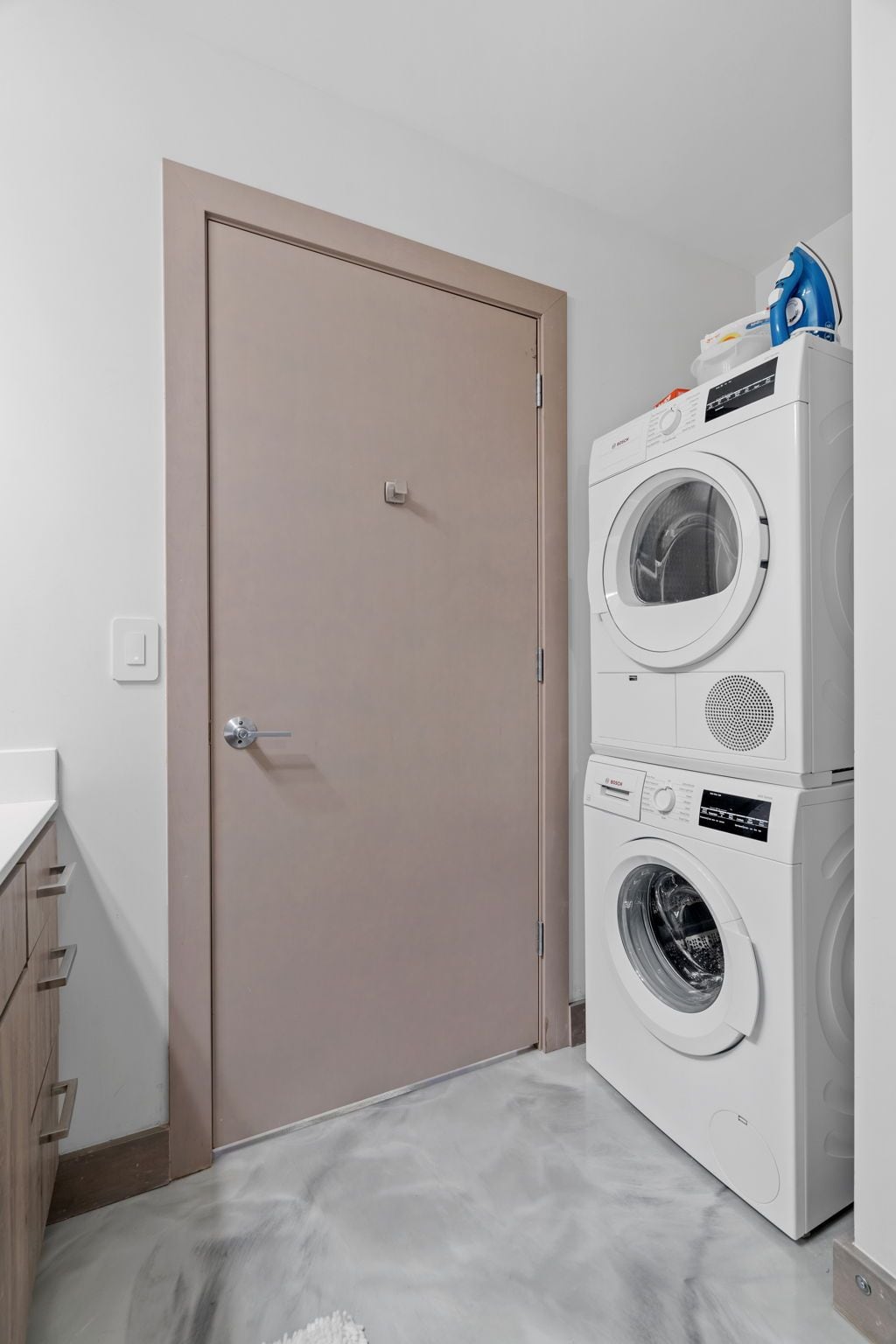 A laundry room with a beige door, a stacked washer and dryer, and a small countertop with a sink.