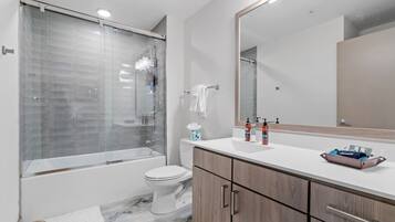 A modern bathroom with a glass-enclosed shower, a white toilet, and a wooden vanity with a mirror.